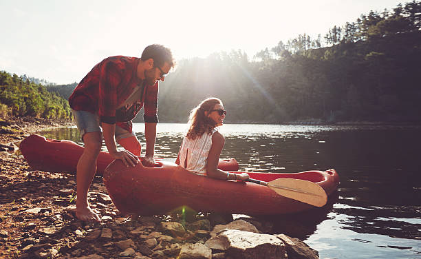 Couple going for kayaking in lake Young man pushes a canoe in the water while a woman sitting on the canoe. Couple going for kayaking in lake on a summer day. kayaking stock pictures, royalty-free photos & images