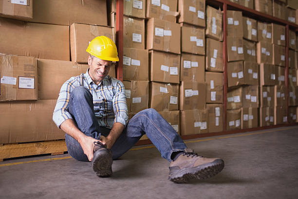 Worker with sprained ankle on floor in warehouse Male worker sitting with sprained ankle on the floor in warehouse physical injury stock pictures, royalty-free photos & images