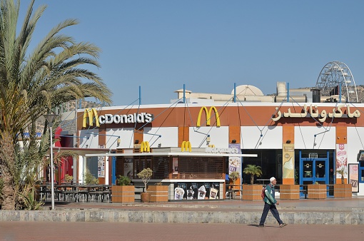 Agar, Morocco - February 17, 2016: McDonalds fast food restaurant in Agadir, Morocco along the Plage D'Agadir with a lone Berber Moroccan man walking by. You also get to see how McDonalds is written in Arabic for no additional cost