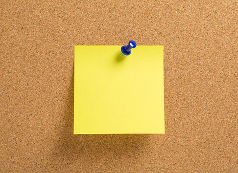 Blank yellow notepaper with blue push pin on a corkboard