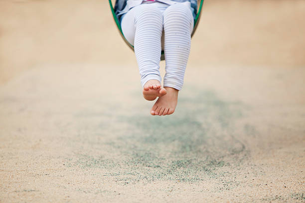 Child is swinging in the park bare feet.