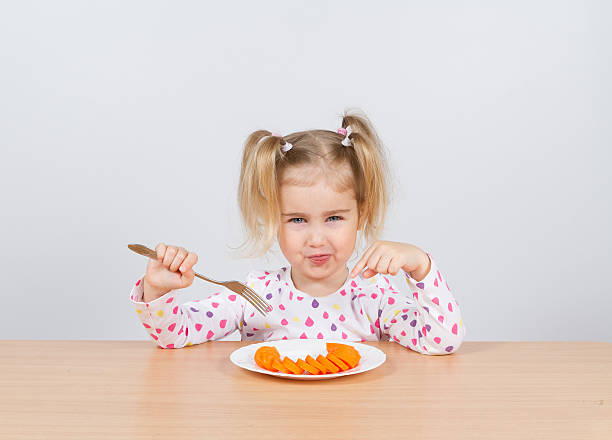 mała dziewczynka jedzenie marchew z widelec. - cute disgust carrot caucasian zdjęcia i obrazy z banku zdjęć