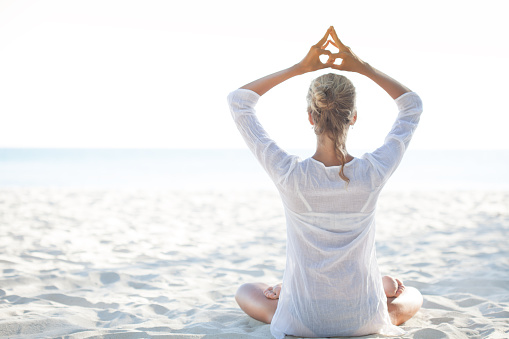 Young woman sitting on the  beach and meditating. Balancing the energy in yoga style. Sea in background.