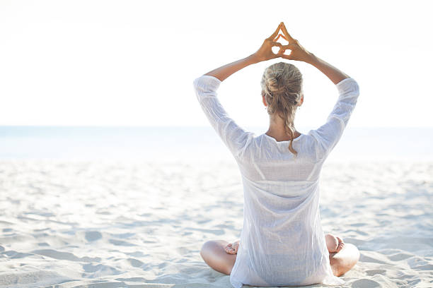 młoda kobieta siedzi na plaży i medytacji - zen like nature breathing exercise sitting zdjęcia i obrazy z banku zdjęć