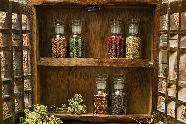 Vintage Wooden Spice Rack or Storage Cabinet Farms vintage Spice Rack or Storage Cabinet: Wall Mount - Display Shelf, Two Drawers, Six Glass Bottles with oregano on rural background village life spice rack stock pictures, royalty-free photos & images