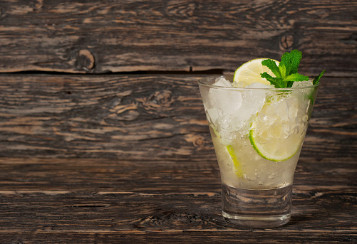 cocktail with white rum or gin with ice, lime and mint on a dark wooden background with copy space. Summer cocktails background