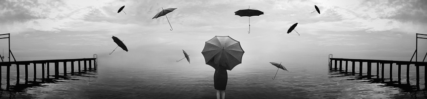 woman in black takes shelter from a surreal rain of umbrellas on the sea
