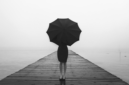 elegant woman dressed in black hiding with umbrella in a misty landscape