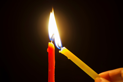 Hand is lighting two candles against dark background