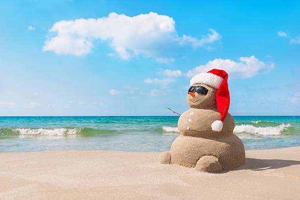 Christmas snowman in santa hat at sandy beach Sandy christmas snowman in red santa hat and sunglasses at sunny beach. Holiday concept for New Years Cards. anthropomorphic smiley face photos stock pictures, royalty-free photos & images