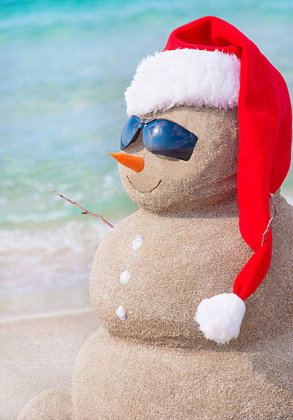 istock Christmas snowman in santa hat at sandy beach 516877735