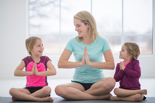 A mother and her daughters are doing yoga together in their home on mother's day. They are sitting and meditating together happily.