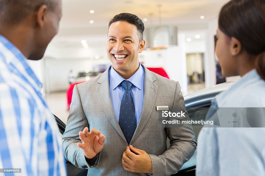 vehicle dealer talking to customers handsome vehicle dealer talking to customers in showroom Name Tag Stock Photo