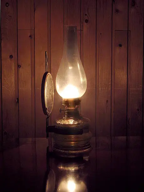 Old oil lamp on the desk and wooden wall in the background.
