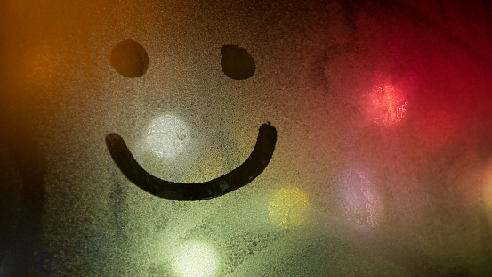 Smiley drawn on the foggy glass on window
