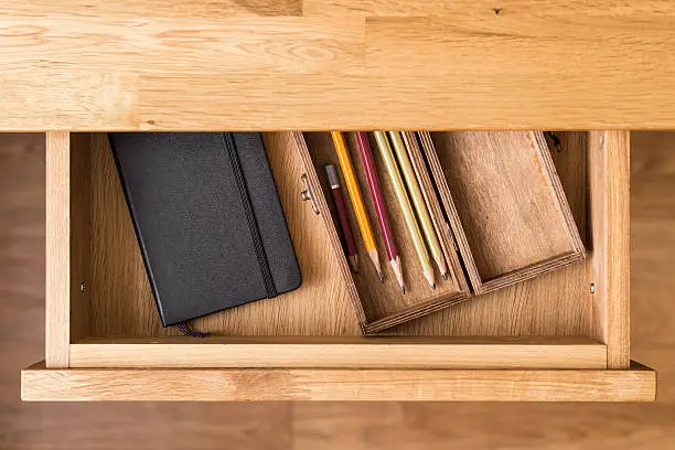 Photo of Notebook and pencils in open desk drawer top view