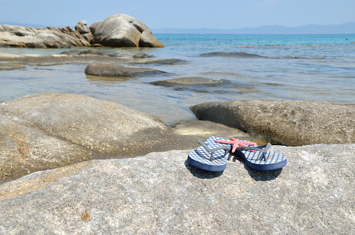 Blue flip flops on sea rock with turquoise sea water in background