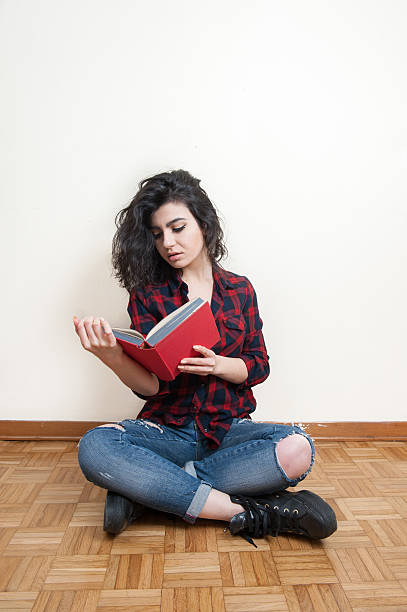 istock Young woman reading a book sitting on the floor 516901876