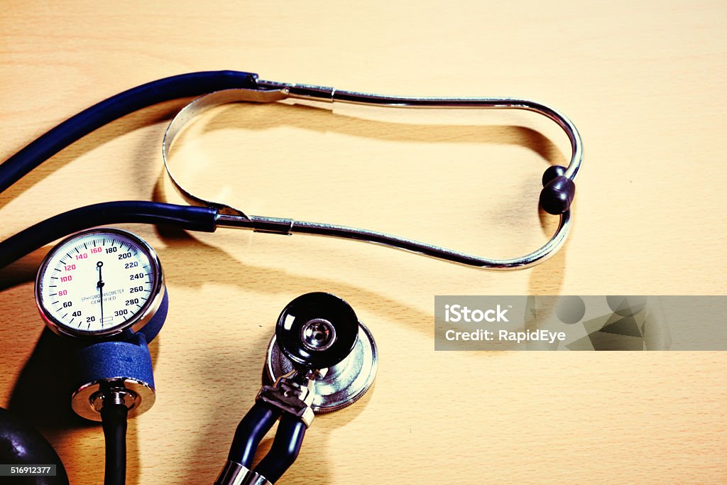 Primary health check equipment: stethoscope and blood pressure gauge A sphygmomanometer on a wooden desk, with a stethoscope alongside. The equipment needed for a basic medical exam. Blood Stock Photo