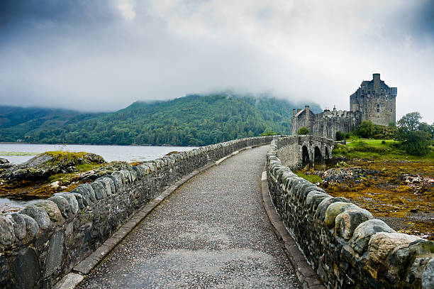 View of Eilean Donan Castle in Scotland Scotland, Uk - August 16, 2005: View of Eilean Donan Castle in cloudy day with dramatic light drawbridge photos stock pictures, royalty-free photos & images