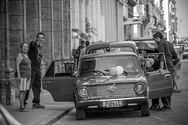 Havana, Cuba - November 10, 2015: Busy weekday in November on downtown street in Havana, Cuba. Vintage Russian car parked on the side of the boulevard. Front end is decorated with balloons. People standing around, some getting out. They all look happy and excited.