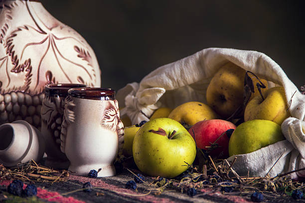Ethnic folklore table covered with national balkan carpet with ethnic ceramic clay jug and ceramic clay glasses for wine and apples.