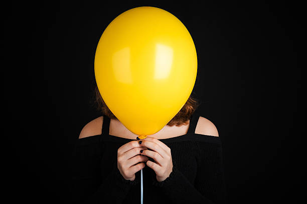 istock Girl hiding her face under yellow balloon 516928026