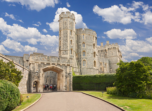 Woodstock, United Kingdom - June 29, 2015: Windsor Castle, Berkshire, England, United Kingdom. The original castle was built in the 11th century and is the longest-occupied palace in Europe. Castle entrance, tourists, green bushes, trees and vivid blue sky with clouds are in the image.