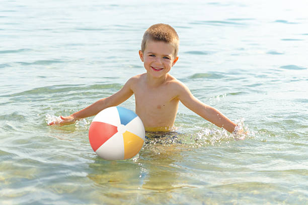 Beautiful boy playing with the beach ball in the sea stock photo