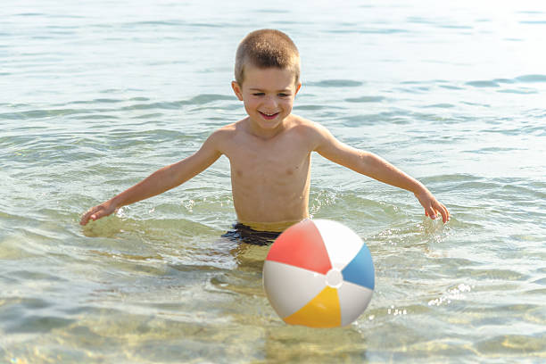 Beautiful boy playing with the beach ball in the sea stock photo