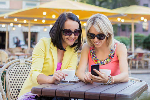 Two cheerful women having friendly chat in cafe and viewing pictures on mobile phone.