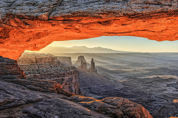 arco laranja ao nascer do sol, a vista para um vale. - canyonlands national park utah mesa arch natural arch - fotografias e filmes do acervo