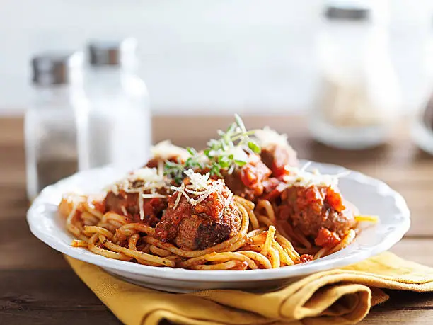 spaghetti and meatballs with oregano garnish on rustic table shot with selective focus