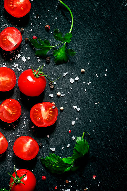 istock Cut cherry tomatoes on a black background with spices 516958644