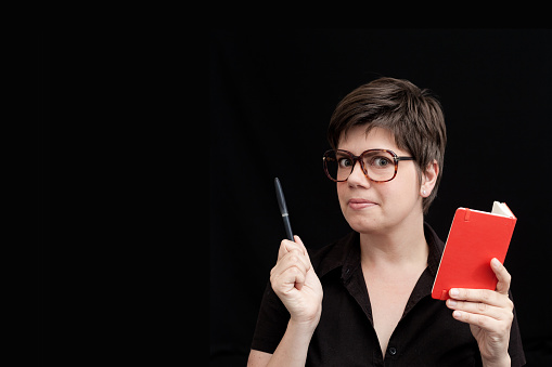 a woman wearing glasses with a red notebook and a black pen on each hand ready to give a lesson