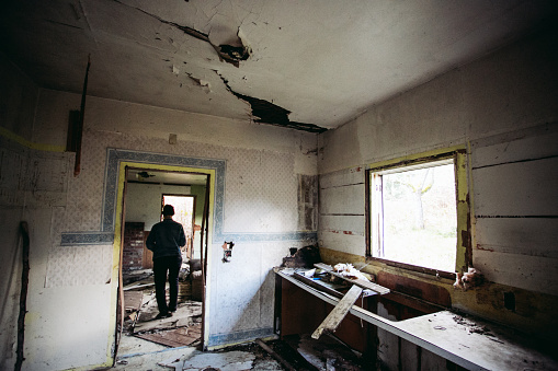 Real lifestyle photo of a young male explorer walking around inside an abandoned home in the middle of a forest. This home was clearly abandoned for many years and has been trashed by squatters over the years. This image shows the young man walking inside the house interested in seeing what might be around the corner.