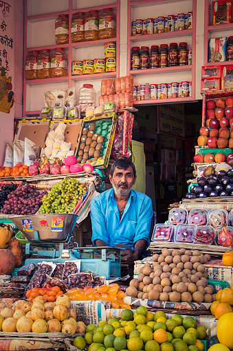 Bikaner, Rajasthan, India – December 14, 2015: An exhausted greengrocer sitting among colorful fruits in his shop.