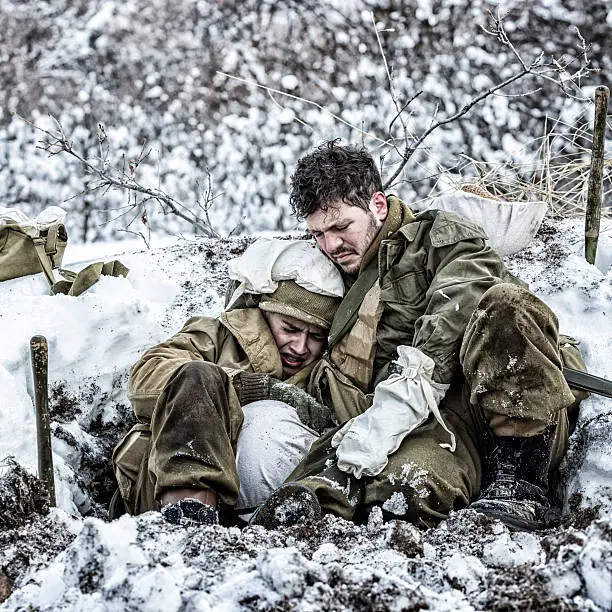 In a frozen foxhole in a winter snow covered bunker, a terrified, helpless young World War II US Army combat infantry soldier is crying. He's being held and comforted by his more seasoned buddy - sadly doing his best to help his traumatized friend, but also struggling to hold it together. Truly "Brothers in Arms". The men are dressed in authentic period-correct uniforms and helmets, and (when applicable in this photo series), they are carrying historically accurate weapons, equipment, tools, medical gear, insignia, etc. Professional reenactment actors/models at the January-February 2016 Utah "WWII US Military Winter Whites" retro revival photo shoot.