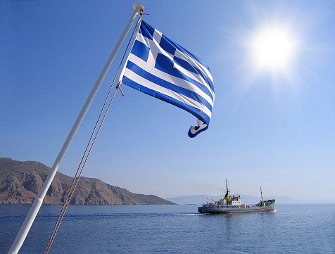 Sea view with greek flag, mountain, sun and cargo ship