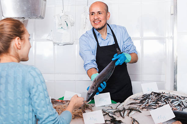 istock Mature  seller helping female customer to choose fish 516981586