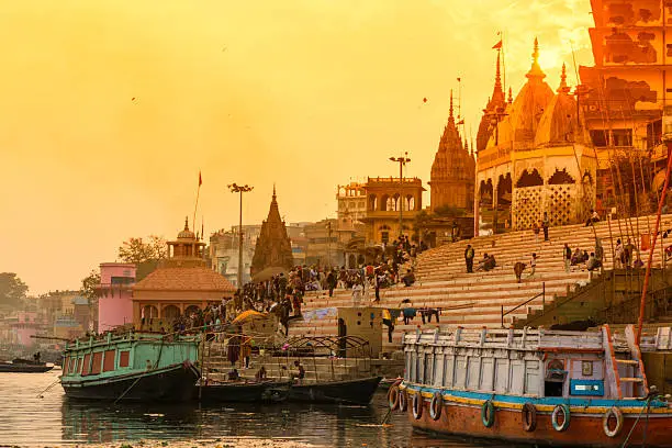 Scenic view from the river on Ghat with crowd. Sunset colores the temples. Varanasi known as Banaras is the holies city in India. It is on the banks of the river Ganges where the special funeral ritual, cremation goes on for purifying and final releases of the spirit from the body.