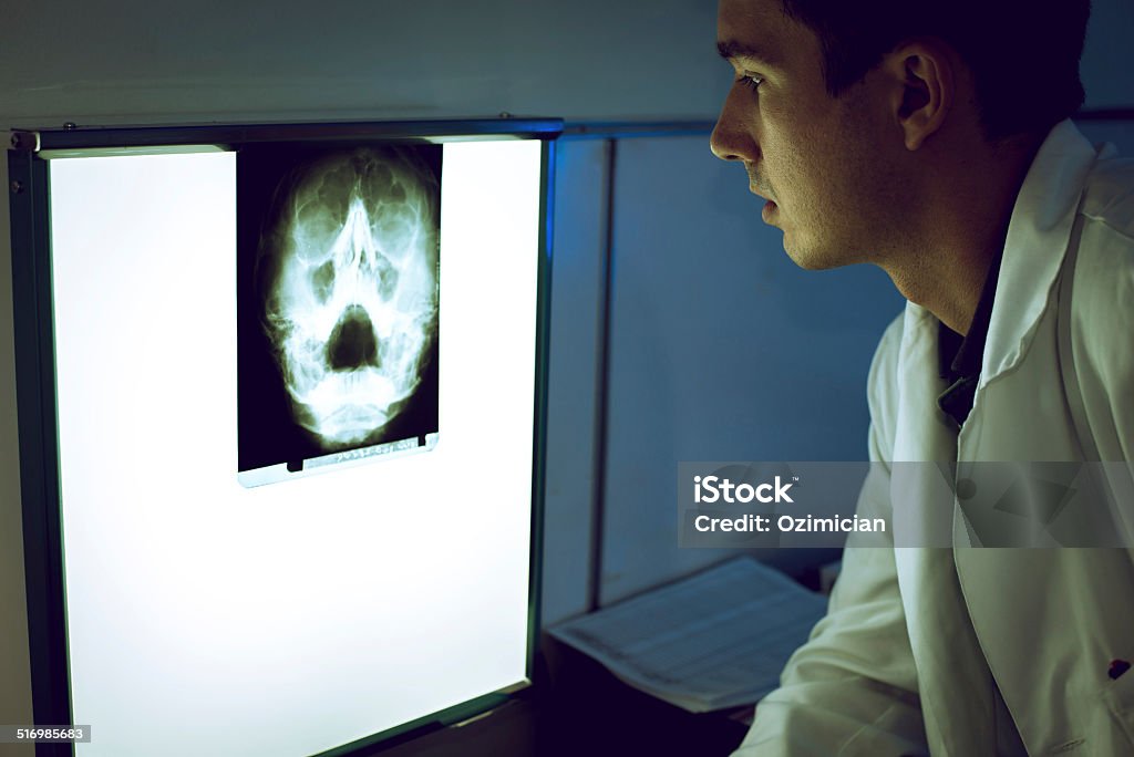 Young doctor looking at X-ray Young doctor taking look at x-ray image on the wall. Doctor Stock Photo