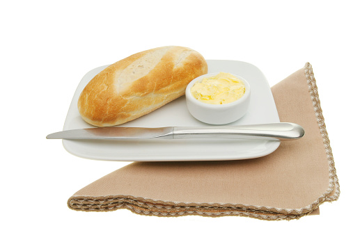 Baguette bread roll with butter and a knife on a plate with a napkin