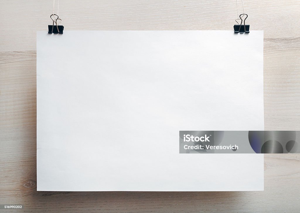 Blank paper poster Photo of blank white paper poster hanging on light wooden background. Mock-up for design presentations and portfolios. Front view. Poster Stock Photo