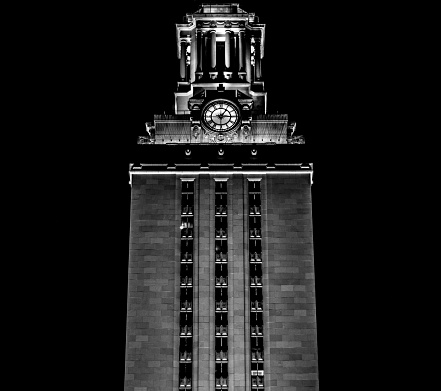 The University of Texas at Austin Main Building, also known as The Tower, lit up at night against a completely black background in black and white.