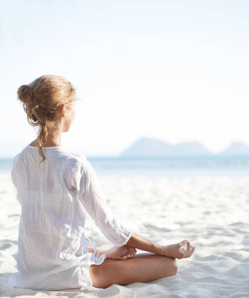 jovem mulher sentada na praia e meditando - zen like nature breathing exercise sitting imagens e fotografias de stock