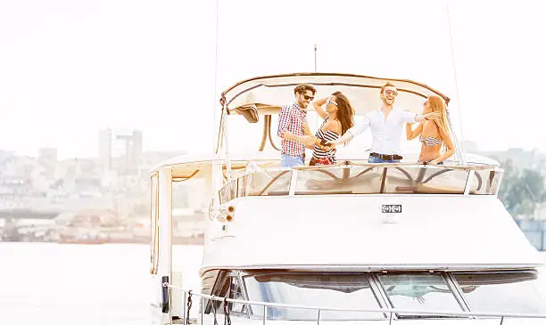 Two young couples enjoy ride on the motor yacht. Selective focus to young woman and man driving yacht.