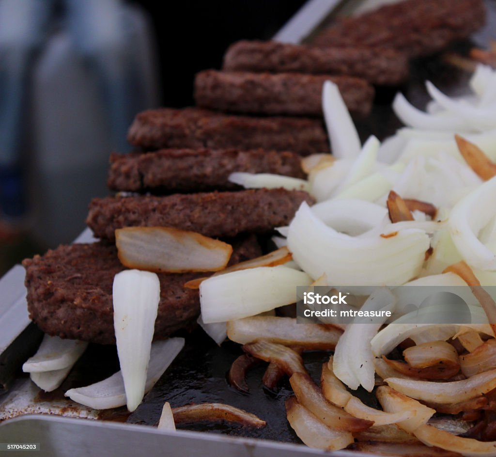 Beef burgers frying, sliced white onions on griddle / grill pan Photo showing a line of beef burgers frying with large slices of white onions, on a stainless steel, commercial grill pan / griddle. Burger Stock Photo