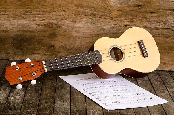 Ukulele and  Paper Chordschart document on wooden background