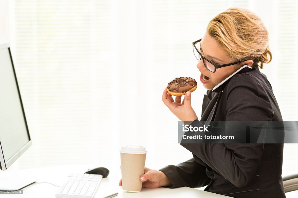 No time for break Businesswoman eating donut at work while using computer and talking on the phone at the same time. Eating Stock Photo